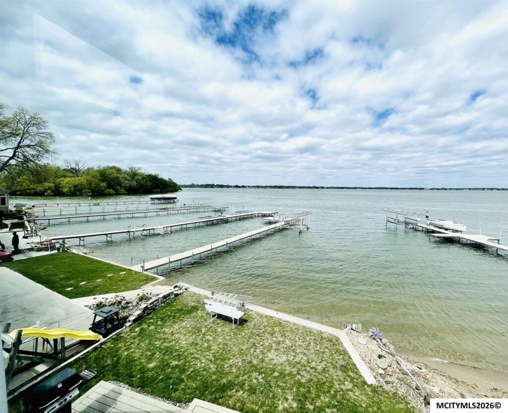 Lakeside marina with multiple docks extending into calm water and a tree-lined shore under partly cloudy sky