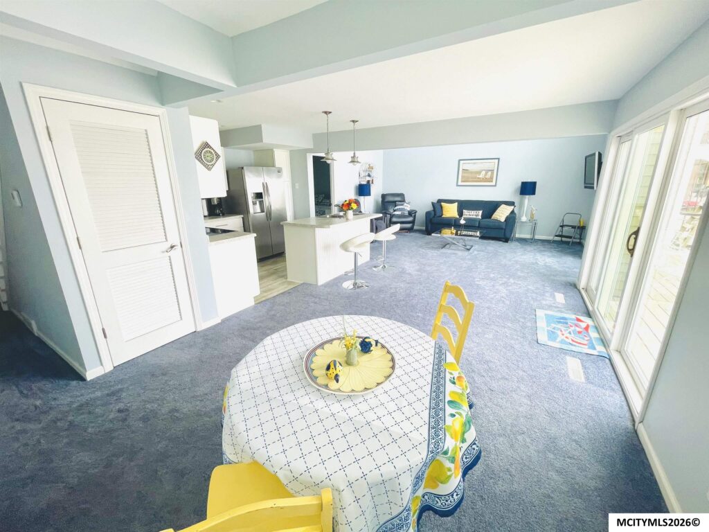 Open-plan living room and kitchen with blue walls, pendant lights, stainless fridge, and glass doors to the outside.